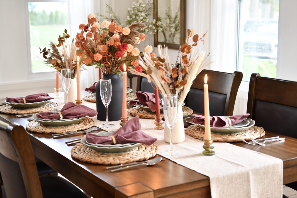 Fall-inspired dining table at Long Lake Memories featuring floral centerpieces, lit taper candles, woven placemats, mauve linen napkins and elegant place settings.
