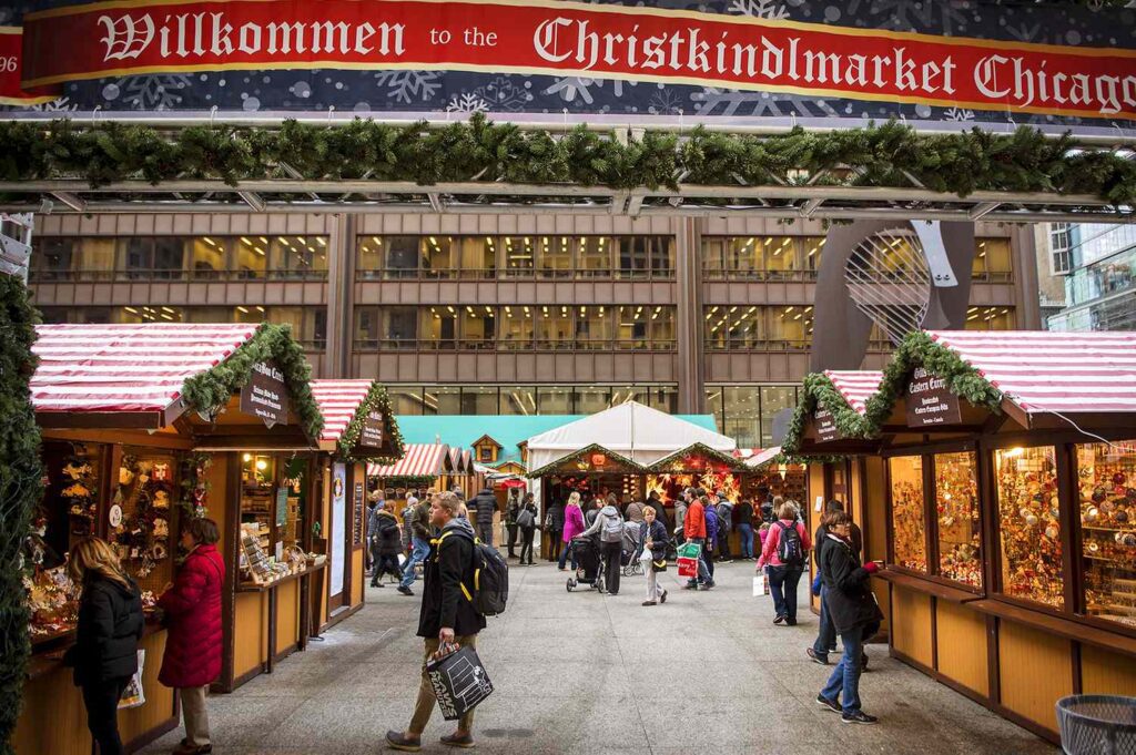 Visitors browse festive wooden vendor stalls decorated with evergreen garlands at Chicago’s Christkindlmarket in Daley Plaza.